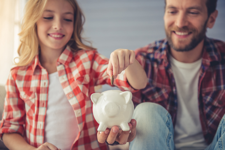 child with father putting money into a piggy bank