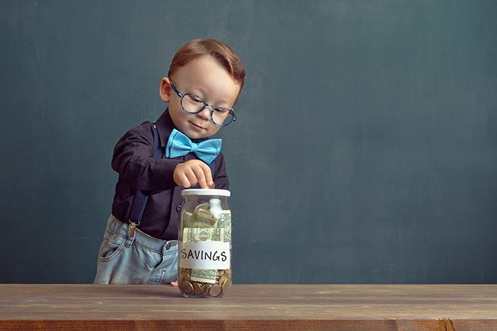 small boy with glasses and bowtie dropping money into a savings jar