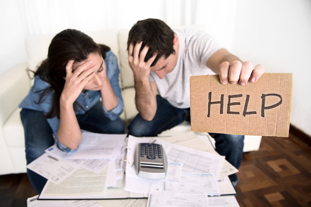 couple looking at bills and holding a help sign