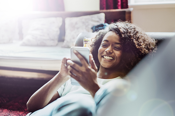 Happy woman using mobile phone on sofa