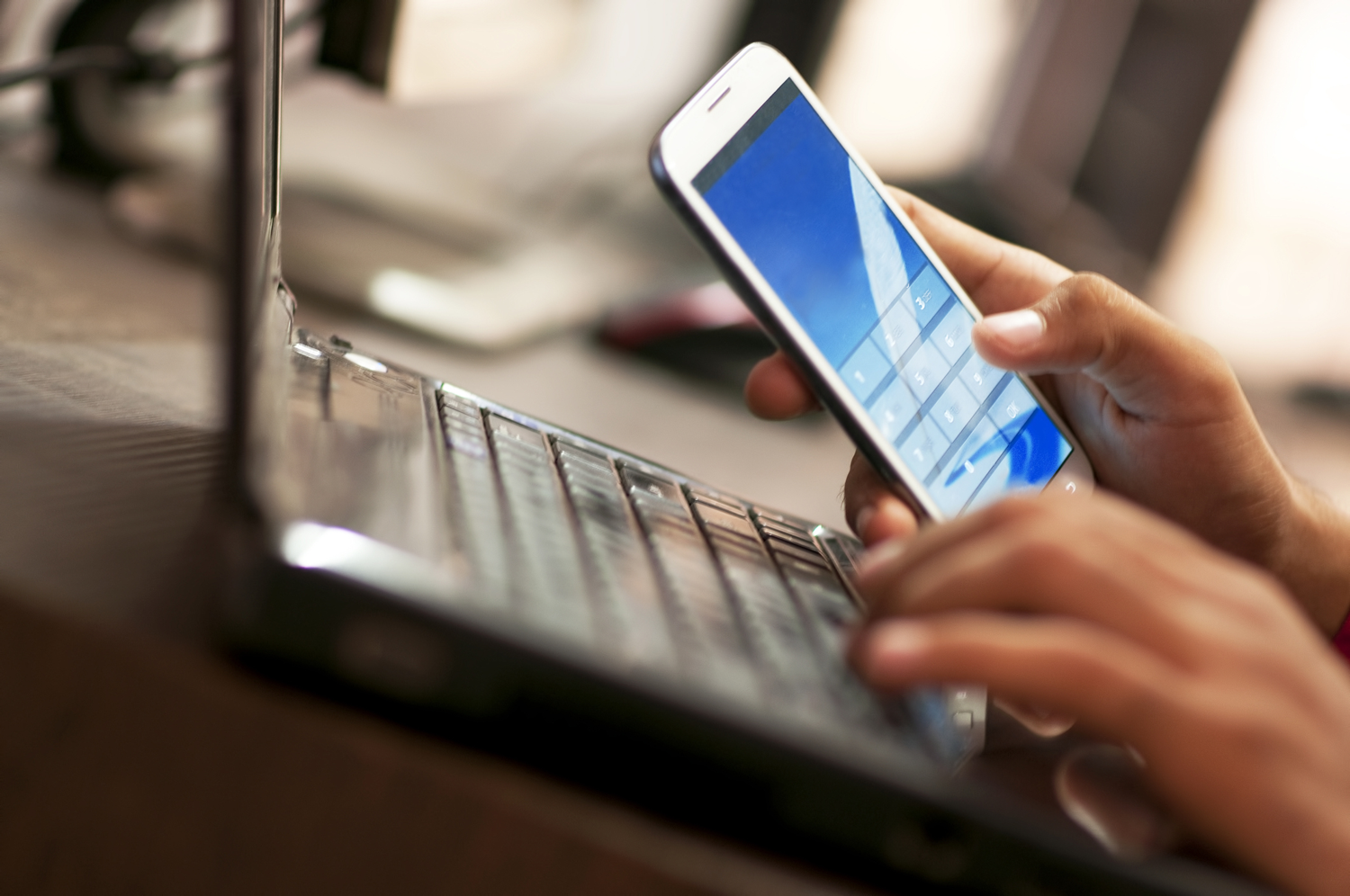 man typing passcode into phone while sitting at laptop