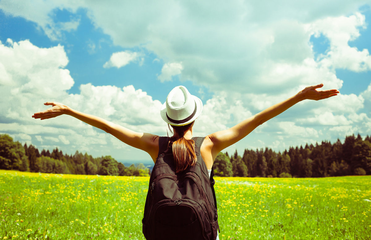 woman with backpack in a field with arms lifted